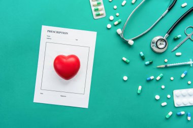 Stetoskop, şırınga, makas ve yeşil zemin üzerinde kırmızı kalp şeklindeki top içeren reçeteler