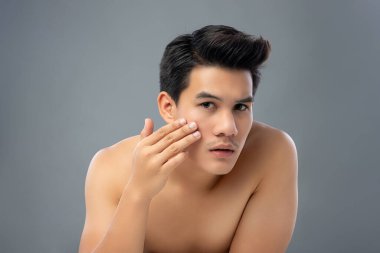 Tişörtsüz yakışıklı Asyalı adamın portresi cilt bakımı ve güzellik konsepti için yüzüne dokunup kontrol ediyor.