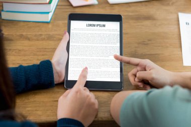 Öğrenciler masadaki e-kitap okuyucu ve eğitim teknolojisi konsepti hakkında bilgi okuyup tartışıyor