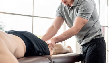 Erkek terapist, klinikte yatakta yatan sporcu hastaya bacak masajı yapıyor. Spor fizyoterapisi konsepti.
