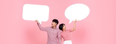 Happy smiling young Asian couple with speech bubbles studio shot on pink banner background clipart