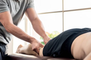 Erkek terapist, klinikte yatakta yatan sporcu hastaya bacak masajı yapıyor. Spor fizyoterapisi konsepti.