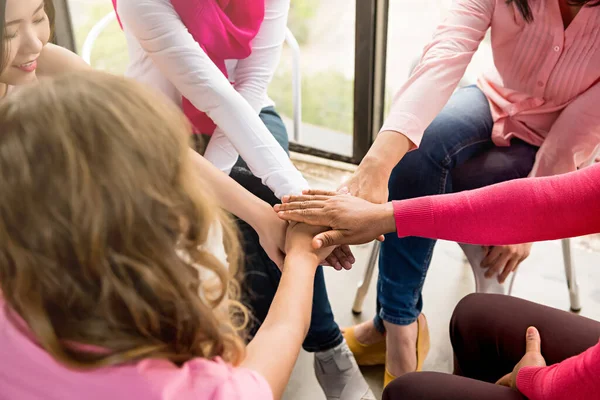 Multiethnic women wearing pink color clothes put their hands together in stack empowering each other in breast cancer awareness campaign meeting
