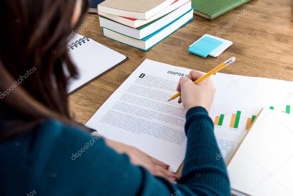 Female college student reading information on paper doing homework assignment at the table