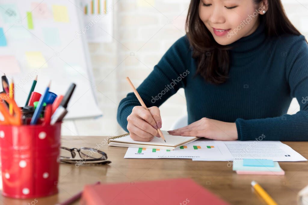 Young Asian female college student writing on notebook doing homework at the table