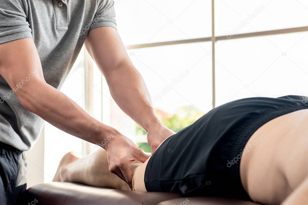 Male therapist giving leg massage to athlete patient on the bed in clinic, sports physical therapy concept