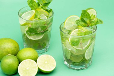 Yeşil arka planda taze dilimlenmiş limon ve nane yapraklarıyla bardaklarda Mojito kokteyli içecekler ferahlatıcı.