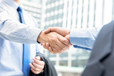 Şehirdeki ofis binalarının önünde tokalaşan iş adamları - selamlama, anlaşma, birleşme ve satın alma kavramları