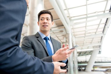 Asyalı Çinli iş adamı, iş arkadaşıyla şehrin gizli geçidinde akıllı telefondan bilgi tartışıyor.