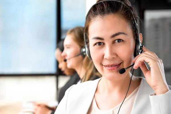 Smiling Asian woman working in call center with international team as telemarketing customer service agents