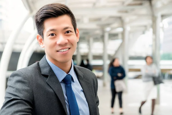 Cheerful handsome Asian Chinese businessman wearing gray suit and blue tie at outdoors covered walkway in the city