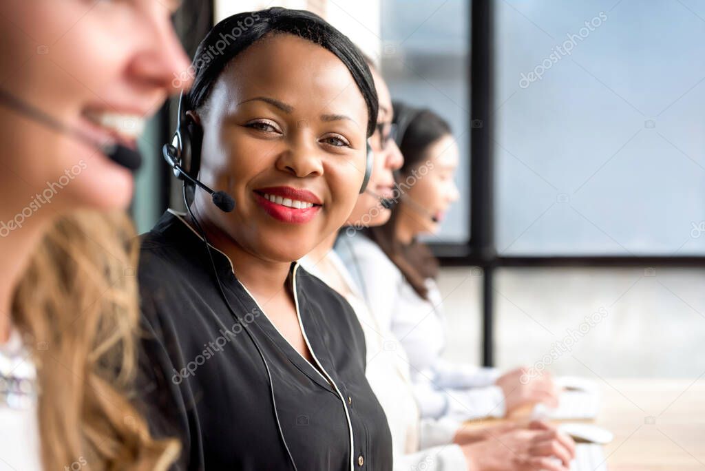 Friendly black woman wearing microphone headset working in call center with international team as telemarketing customer service agents