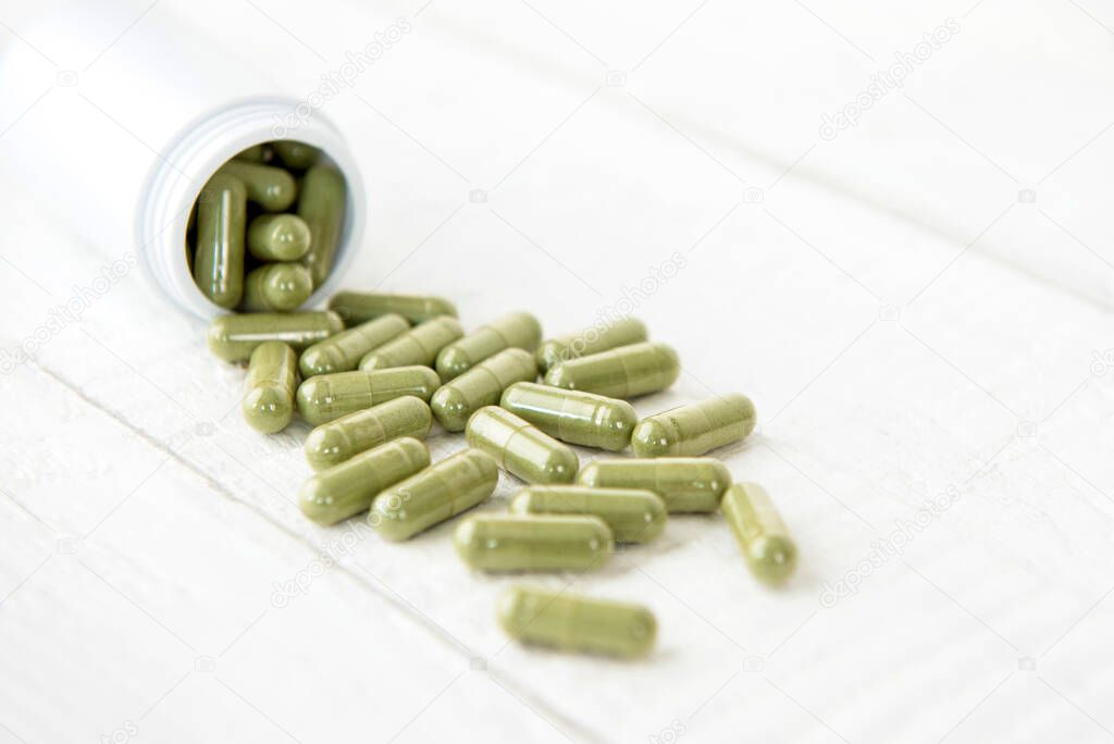 Close up of organic natural green Asian Kariyat plant herbal extract medicine in form of capsules spillig out of the bottle