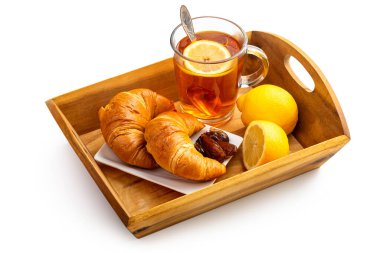 Cam bardakta limonlu çay, kruvasan ve ahşap tepside hurma. Beyaz arkaplanda izole et