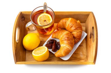 Cam bardakta limonlu çay, kruvasan ve ahşap tepside hurma. Beyaz arkaplanda izole et