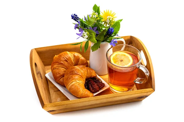 Cam bardakta limon çayı, bir buket kır çiçeği, kruvasan ve tahta tepside hurma. Beyaz arkaplanda izole et