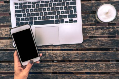 Dizüstü bilgisayarının boş ve anahtarlığıyla telefonu tutan bir kadının üst görüntüsü..