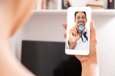 Elinde telefon olan bir kadın ve evdeki bir doktorla internetten web kamerası kullanan bir kadın.