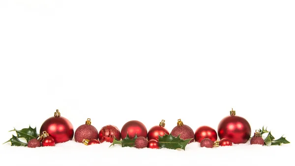 Reihe roter Weihnachtskugeldekorationen und grüner Stechpalme im Schnee — Stockfoto