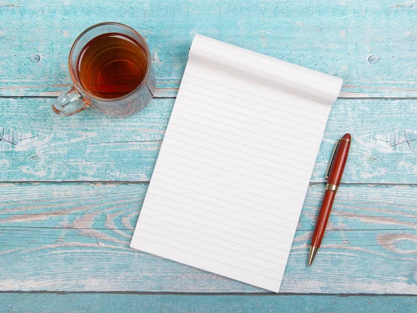 Empty notebook paper with a cup of thee and a pen on a blue wooden table seen from above with space for text