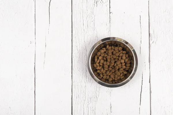 Bol avec des croquettes de chien vu d'en haut sur des planches de bois blanc — Photo