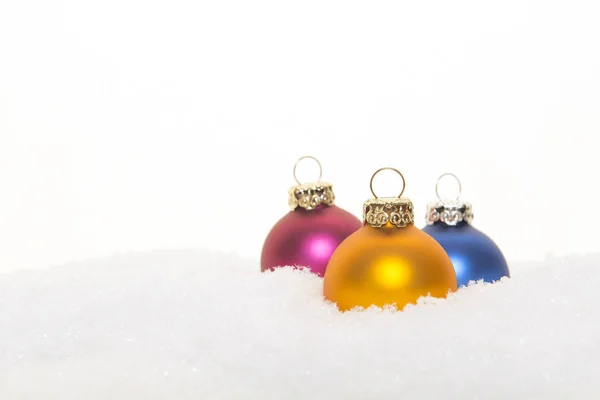Drei bunte Weihnachtskugeln im Schnee auf weißem Hintergrund — Stockfoto