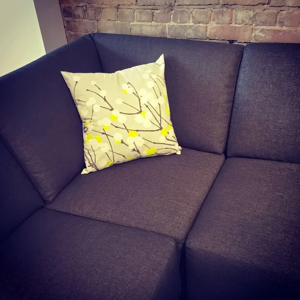 Corner sofa with cushion near brick wall