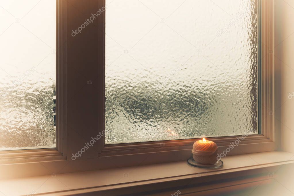 Burning candle and frosted window in hazy light