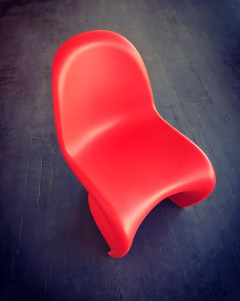 Красный пластиковый стул на темном деревянном полу — стоковое фото