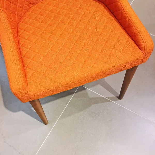 Bright orange armchair on tile floor