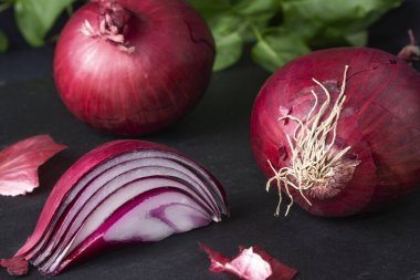 İki soğan, bir dilim ve arka planda yeşil yapraklar. Yatay görüş. Renk karşıtlığı.