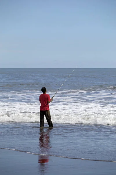 Man fishing on the beach with a long pole