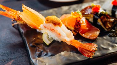 Premium Suşi Seti, wasabi ve pembe salamura zencefil ile servis edilen Siyah Taş Tabakta Deniz Kestanesi, Foie Gras, Somon ve Engawa ile Derin kızarmış Karides içerir. Karides Suşi'de yakın çekim.