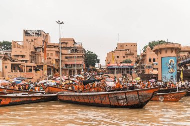 Varanasi, Uttar Pradesh, Hindistan 'da Ganj (Ganga) nehri kıyısında arka planda eski binalarla Ghat' ta yaşayan Hintli insanların yüzen tekneleri ve çeşitliliği.