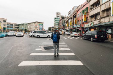 Tourist walks on a crosswalk in Yehliu fisherman village downtown area with road and buildings in northern Taipei. clipart
