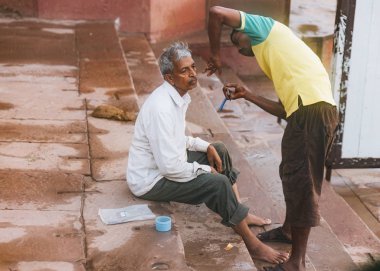 Hintli berber ghat üzerinde bir Hindu hacıyı tıraş eder. Varanasi, Uttar Pradesh, Hindistan 'da Ganj nehri boyunca yaşam..