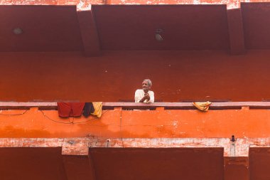 Indian senior standing at the ghat in old red buildings along the Ganges (Ganga) river in Varanasi, Uttar Pradesh, India.