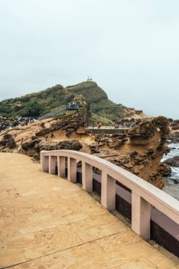 Diversity of tourists walking in Yehliu Geopark, a cape on the north coast of Taiwan. A landscape of honeycomb and mushroom rocks eroded by the sea. Close up on stone bridge.