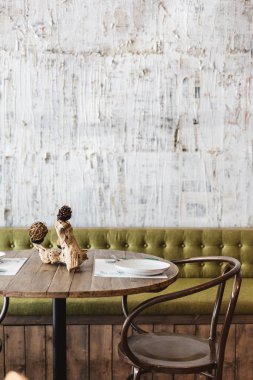 Yemek salonu yeşil kanepe, ahşap masa, siyah çelik sandalye ve beyaz çizik desenli duvar kağıdı ile süslenmiş. Modern restoran atmosferi.