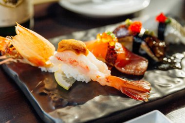 En iyi sushi seti, wasabi ve pembe turşulu zencefil ile servis edilen The Black Stone Plate 'de Sea Urchin, Foie Gras, Somon ve Engawa ile Deep Fried Shrimp' i içerir. Karides Suşi 'ye yakın çekim.