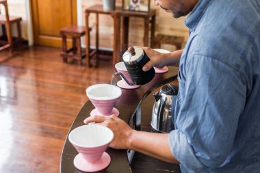 Barista, Damlatma adında alternatif bir metodla kahve yapıyor. Kahve öğütücüsü, kahve standı ve ahşap tezgahın üzerine dökülmüş..