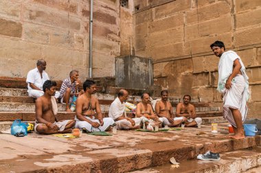 Varanasi, Uttar Pradesh, Hindistan 'daki Ganj (Ganga) nehri boyunca arka planda eski tuğla binalarla ghat' ta yaşayan Hintli Hindu rahiplerin çeşitliliği.