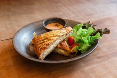 Bin Ada Sosu ve Salata ile servis edilen ızgara Peynirli Sandviç. Yeşil Meşe ve Domates de dahil. Seramik tabakta..