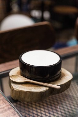 Japon füzyon tatlısı, beyaz sütlü puding. Tahta kaşıkla kereste üzerinde siyah bir seramik kasede servis yap.. 