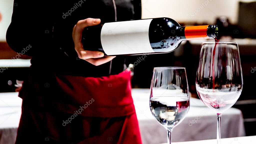 Crop image of Sommelier pouring perfect red wine in a wine glass for celebrating a special occasion. Luxury event with partners.