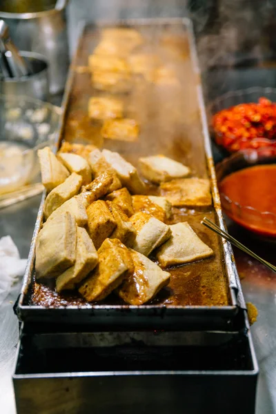Close-up golden Fermented Tofu or Stinky Tofu on a hot plate with chili pepper spicy sauce, famous Taiwanese signature street food eatery at Jiufen, Taiwan.