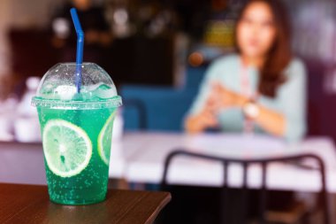 Tahta masada dilimlenmiş limonlu buzlu yeşil İtalyan gazozu. Bulanık kadınla seçmeli soğuk içecek menüsü.