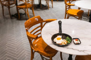 Bibimbap (kimchi domuz eti, yosun ve susamlı kızarmış sebzeyle karıştırılmış Kore pirinci) mermer yuvarlak masada sıcak tavada servis edilir..