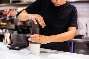 Aero press sistemi kahve hazırlama yöntemi. Siyah tişörtlü kadın barista mermer tezgahtaki espresso kahvesiyle doldurmak için Aeropress 'e baskı yapıyor. Profesyonel kahve imalathanesi..