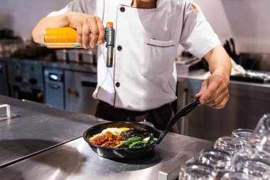 Bibimbap (Kore pilavı kimchi, yosun ve susamlı kızarmış sebzeyle karıştırılmış) sıcak tavada servis edilen şefin kızarmış yumurtanın üzerinde mozzarella peyniri eritmek için kaynak makinesi kullanması..